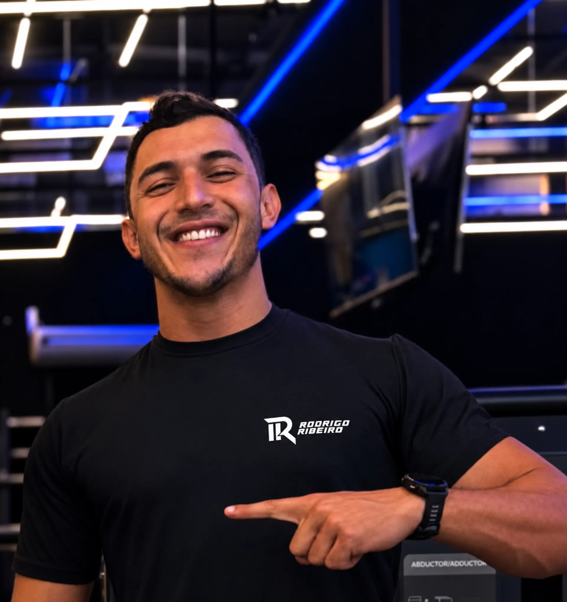 Rodrigo Ribeiro smiling at the gym, wearing his white logo on a black T-shirt